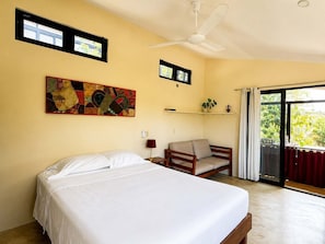 A bedroom with a bed, a chair, a ceiling fan, a window, and a wall-mounted shelf. - Bungalow doble, cama Queen, cocina completa (Cuatunalco)