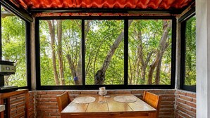 Un comedor con pared de ladrillo, una mesa de madera y sillas, con un amplio ventanal que ofrece vistas a árboles.