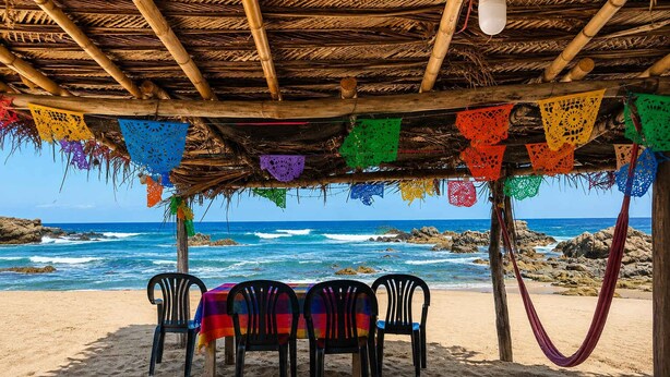 Un área de comedor junto a la playa, con techo de paja, decoraciones de papel de colores y vistas al océano.