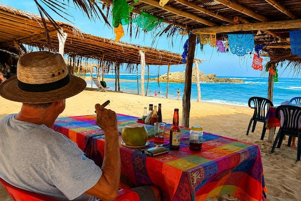 A beach scene with a table set for two, featuring a colorful tablecloth and various bottles.