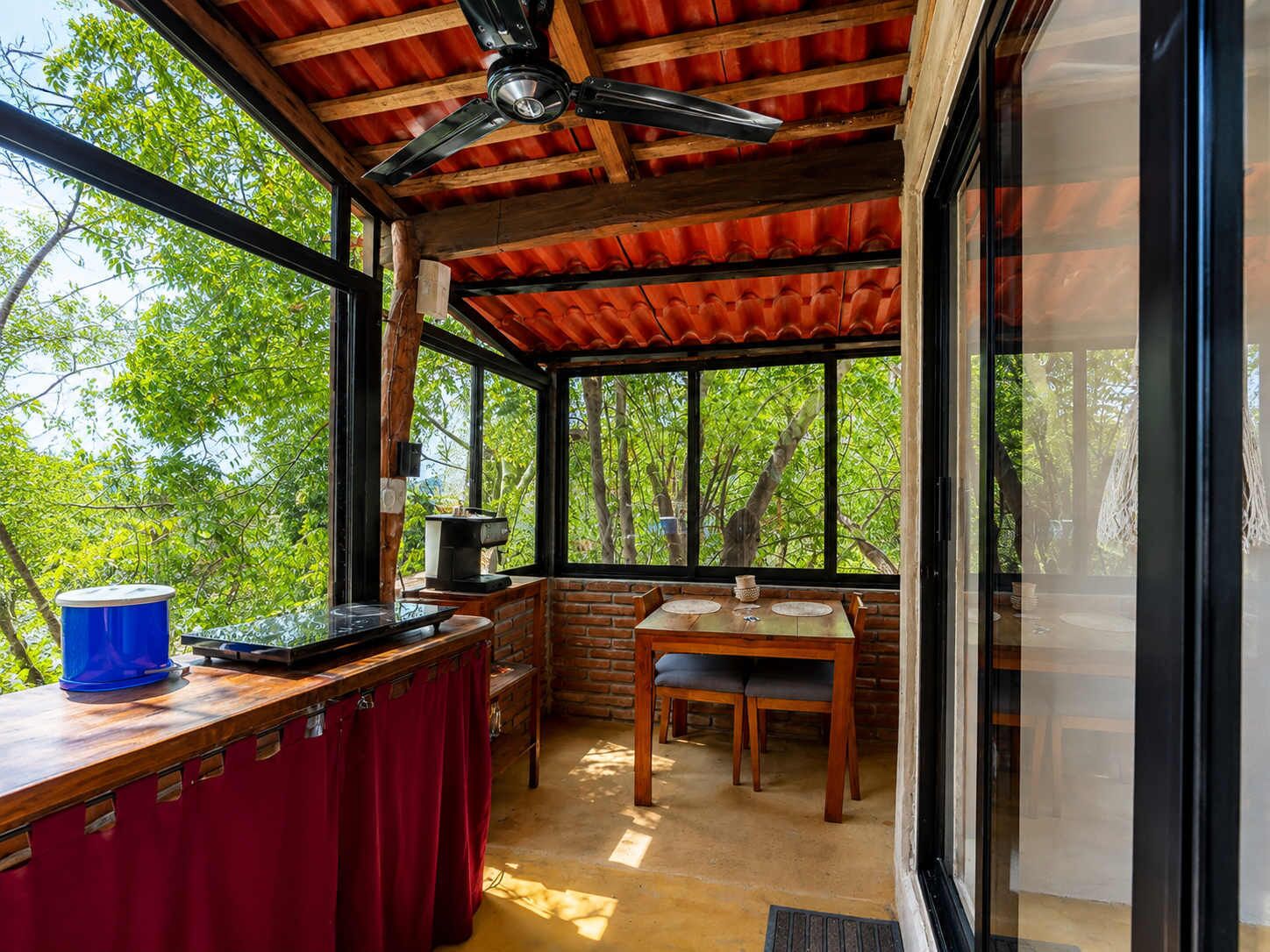 Ein Zimmer mit Holzbalkendecke, einem Tisch mit Stühlen und einem großen Fenster mit Blick auf Grünflächen.