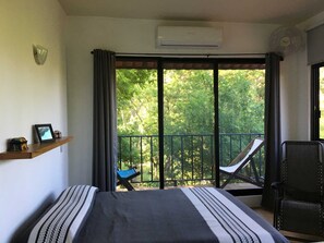 Ein Schlafzimmer mit einem Bett, einem Sessel, einem Regal mit Gegenständen und einem Balkon mit Stuhl und Tisch.