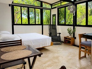 A room with a bed, a chair, a table, and a fan. - Bungalow doble, cama Queen, cocina completa. (Cuatunalco)