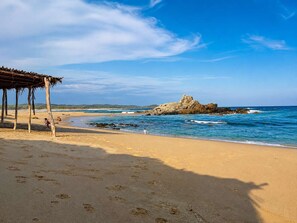 A beach with a rocky outcrop, a wooden structure, and footprints in the sand. - Bungalow doble, cama Queen, cocina completa. (Cuatunalco)