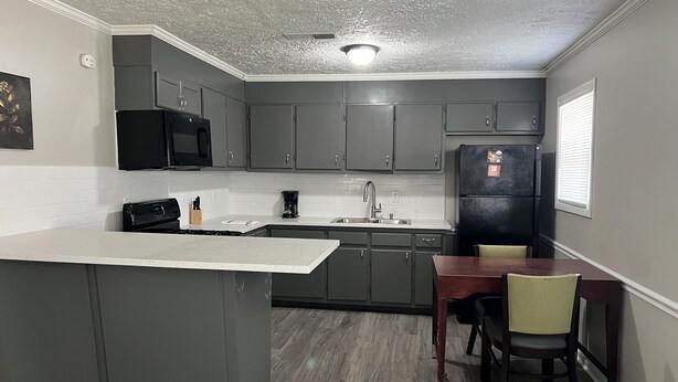 A kitchen with grey cabinets, a black refrigerator, a coffee maker, and a dining table with chairs.