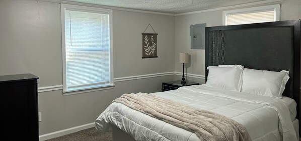 Un dormitorio con cama, mesita de noche, lámpara y un enchufe en la pared.