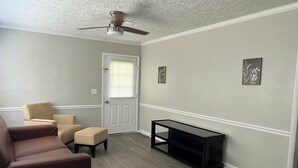 A room with a ceiling fan, a door with a window, a beige sofa, a small round table, and a black console table.