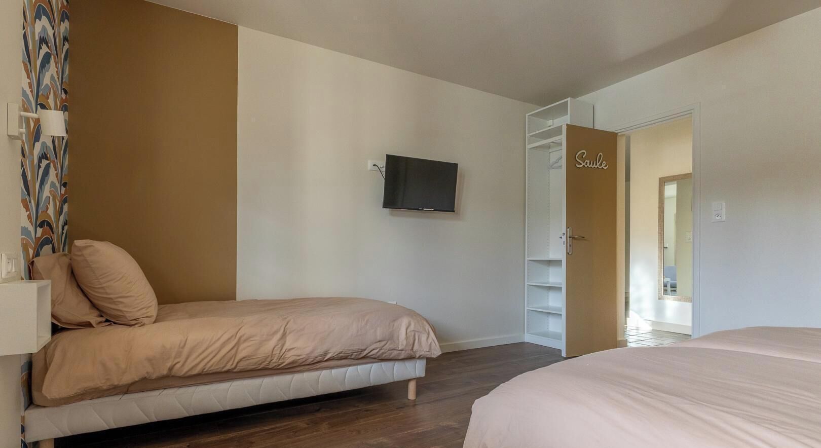 Een slaapkamer met een bed, een televisie, een kledingkast en een deur met de tekst 'Saulé'.