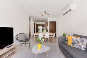A modern living room with a flat-screen TV, a dining area with a table and chairs, a gray sofa with decorative pillows, and a ceiling fan. - Beautiful, modern and spacious on Long Island. Pool view and 24/7 security (Cancún)