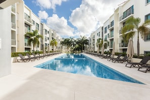 A swimming pool with lounge chairs and palm trees, surrounded by modern buildings. - Beautiful, modern and spacious on Long Island. Pool view and 24/7 security (Cancún)