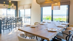 Een eetgedeelte met een grote tafel voor zes personen, omringd door stoelen, met uitzicht op de zee door grote ramen.