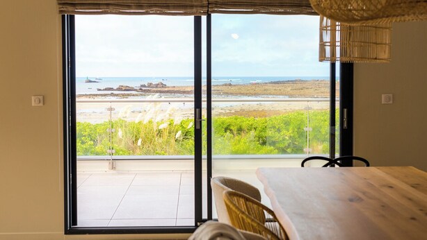 Een kamer met een grote schuifglazen deur die uitkomt op een balkon met uitzicht op een strand en de oceaan.