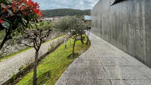 Un sentier dallé de pierres, un mur en béton et une vue sur un paysage vallonné avec des bâtiments visibles au loin.