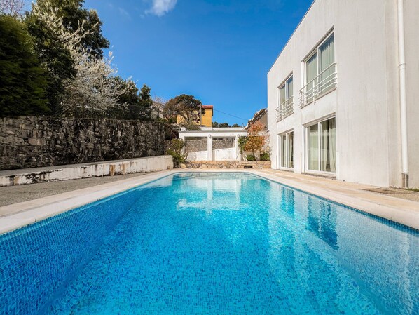 Une piscine avec un mur en pierre et un bâtiment moderne en arrière-plan.