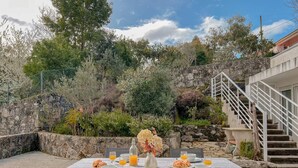Un espace extérieur aménagé pour les repas, avec un mur en pierre, un escalier et diverses plantes.