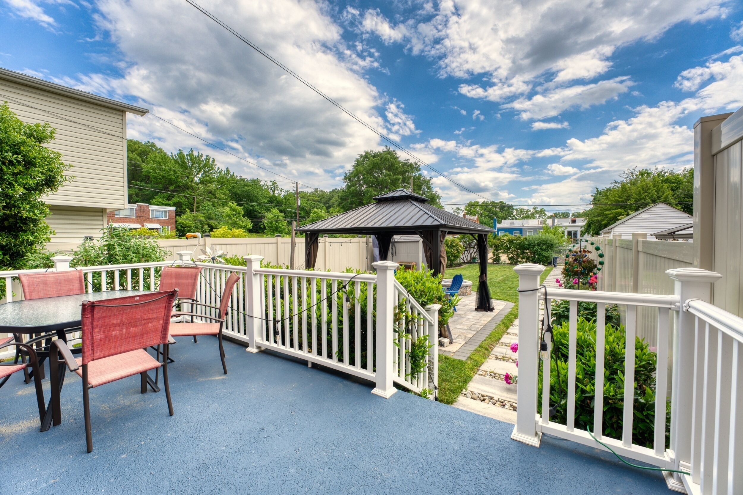 Une terrasse avec une table et des chaises, un belvédère et une clôture blanche.