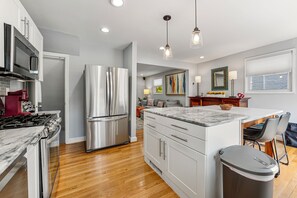 A modern kitchen with stainless steel appliances, a marble countertop island, and a dining area with a sofa and chairs. - Spacious 3BR/2.5BA · Fenced Backyard Oasis · Pets OK (Washington)
