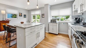 A modern kitchen with white cabinetry, a marble countertop island, and a large window. - Spacious 3BR/2.5BA · Fenced Backyard Oasis · Pets OK (Washington)