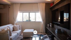 Een moderne woonkamer met een bank, een bijzettafeltje, een televisie en een raam met gordijnen.