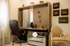 Una taula d'oficina moderna amb un mirall gran, una cadira d'oficina negra, una cadira blanca amb coixí i un calaix penjat a la paret per al teclat amb les tecles 'Ctrl', 'Alt', 'Del' i 'Enter'.