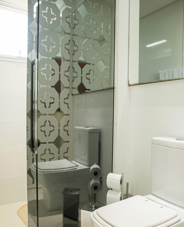 A modern bathroom with a glass shower enclosure, a toilet, and a bidet. - Apartamento Simon Vista Mar - Imbituba (Imbituba)