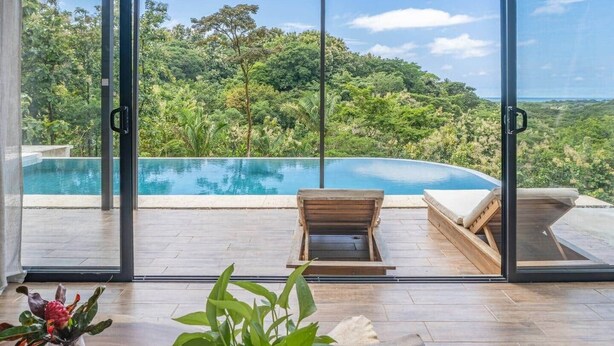 A glass-enclosed room with a pool and a view of a forested landscape. - Brand-New Jungle Hideaway with Ocean View (Sámara)