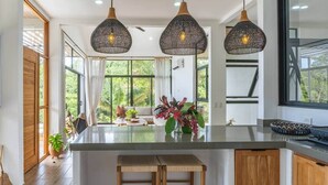 A kitchen with a central island, pendant lights, and a view of greenery outside. - Brand-New Jungle Hideaway with Ocean View (Sámara)
