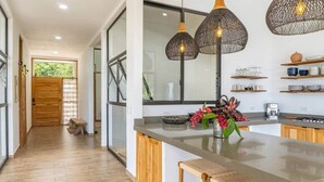A modern kitchen with a central island, pendant lights, and a view through a glass door. - Brand-New Jungle Hideaway with Ocean View (Sámara)