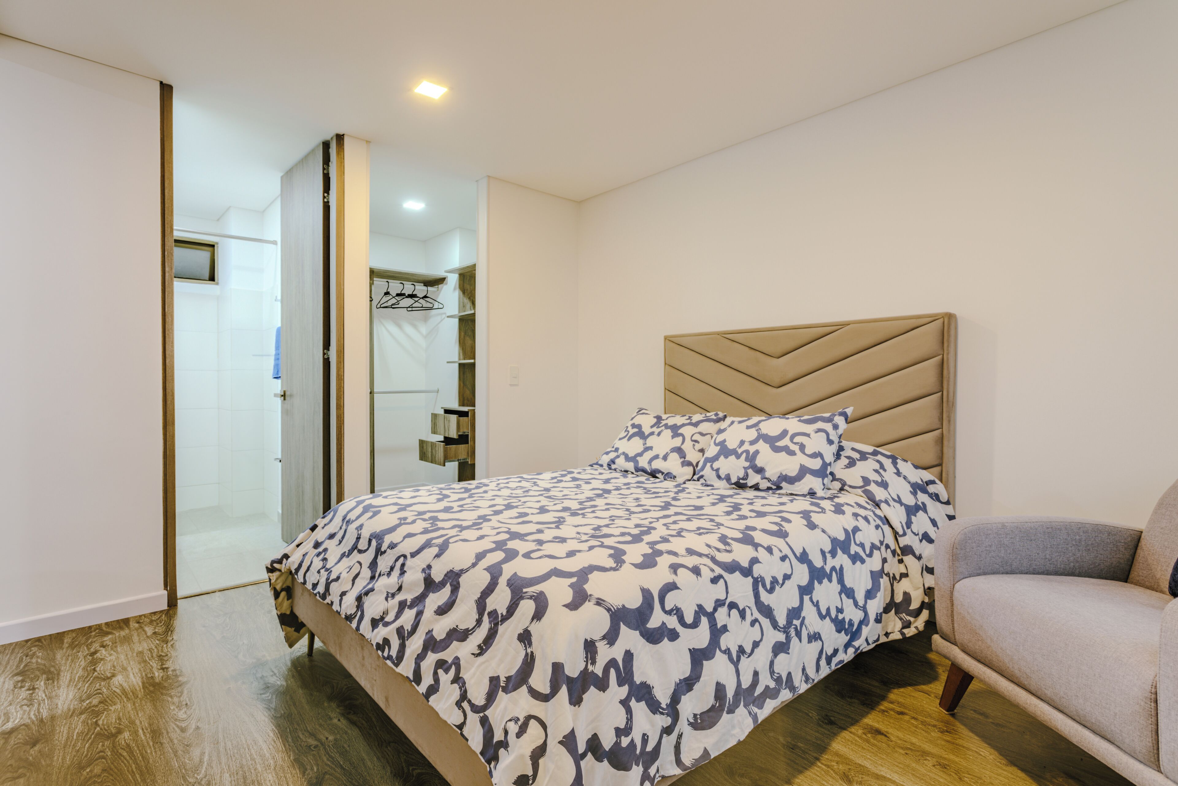 A bedroom with a bed, a chair, a wardrobe, and a mirror.