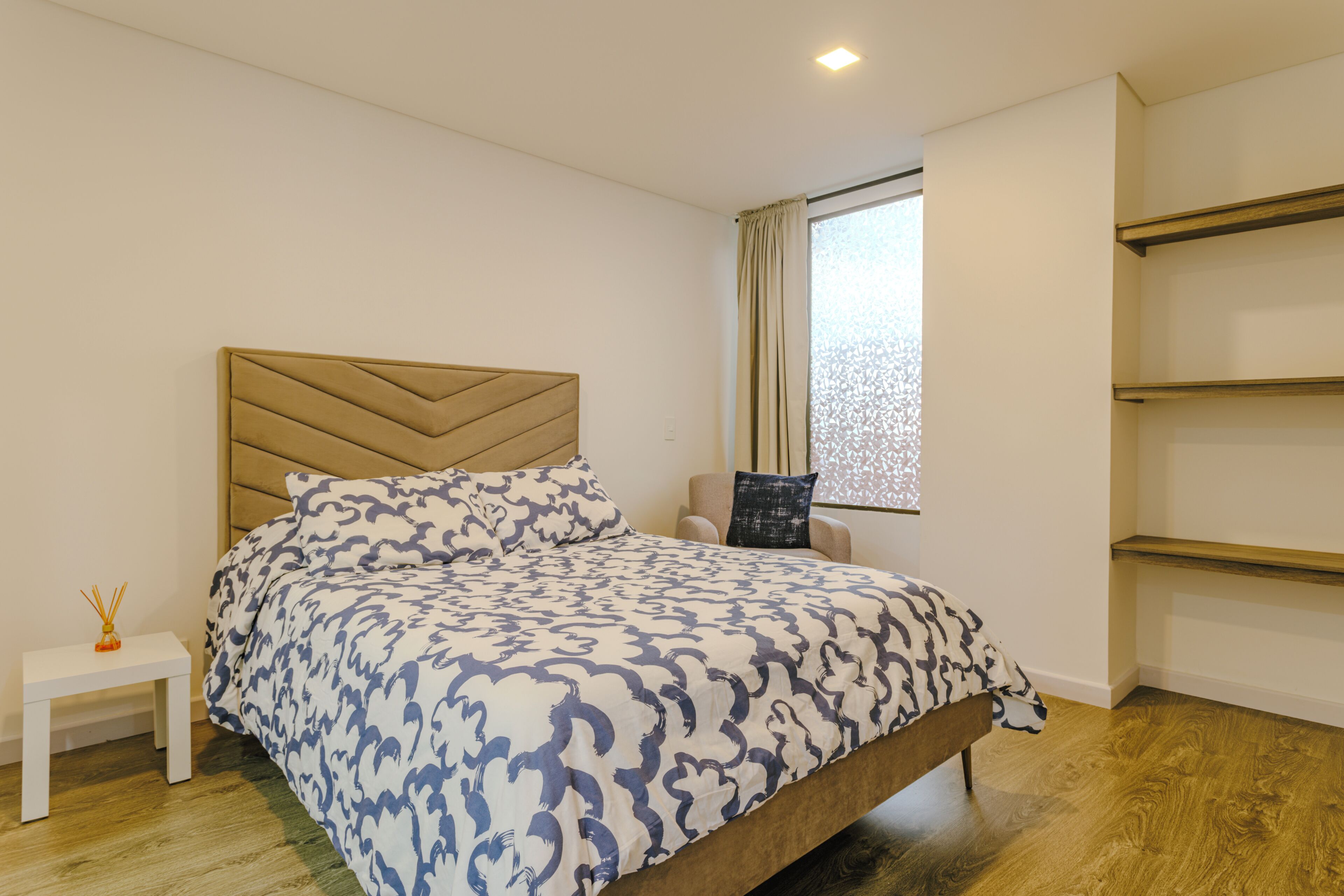 A bedroom with a bed, a nightstand, a window with curtains, and built-in shelves.