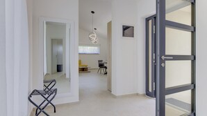 Um corredor com uma porta que dá para um quarto, uma pequena mesa com cadeiras e um lustre.