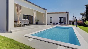Piscina com solário, área de estar externa e um pequeno edifício com janelas.
