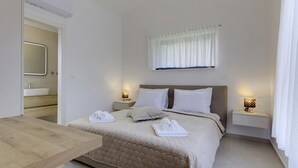 Quarto com cama, mesas de cabeceira, espelho e banheiro visível através de uma porta aberta.