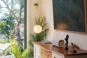 A room with a wooden desk, a globe, a small statue, a wall-mounted lamp, and a large window with a view of trees. - Studio 216 @Bruny ~Romantic, Beachfront & Secluded (Alonnah)