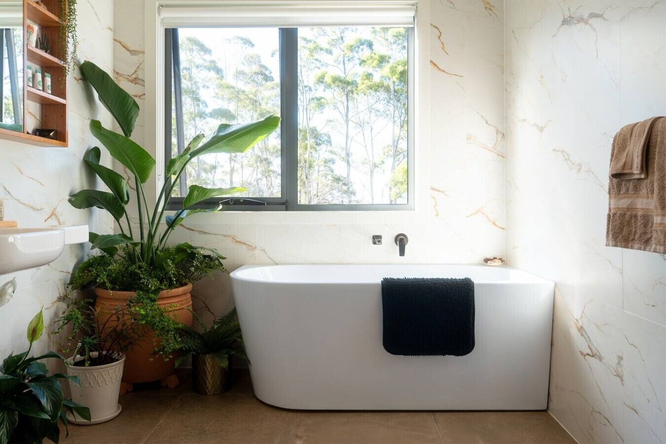 Un baño con una bañera independiente, una ventana y diversas plantas en macetas.