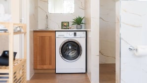 Un espace buanderie compact comprenant un lave-linge, un meuble en bois, une petite plante en pot et un mur en marbre.
