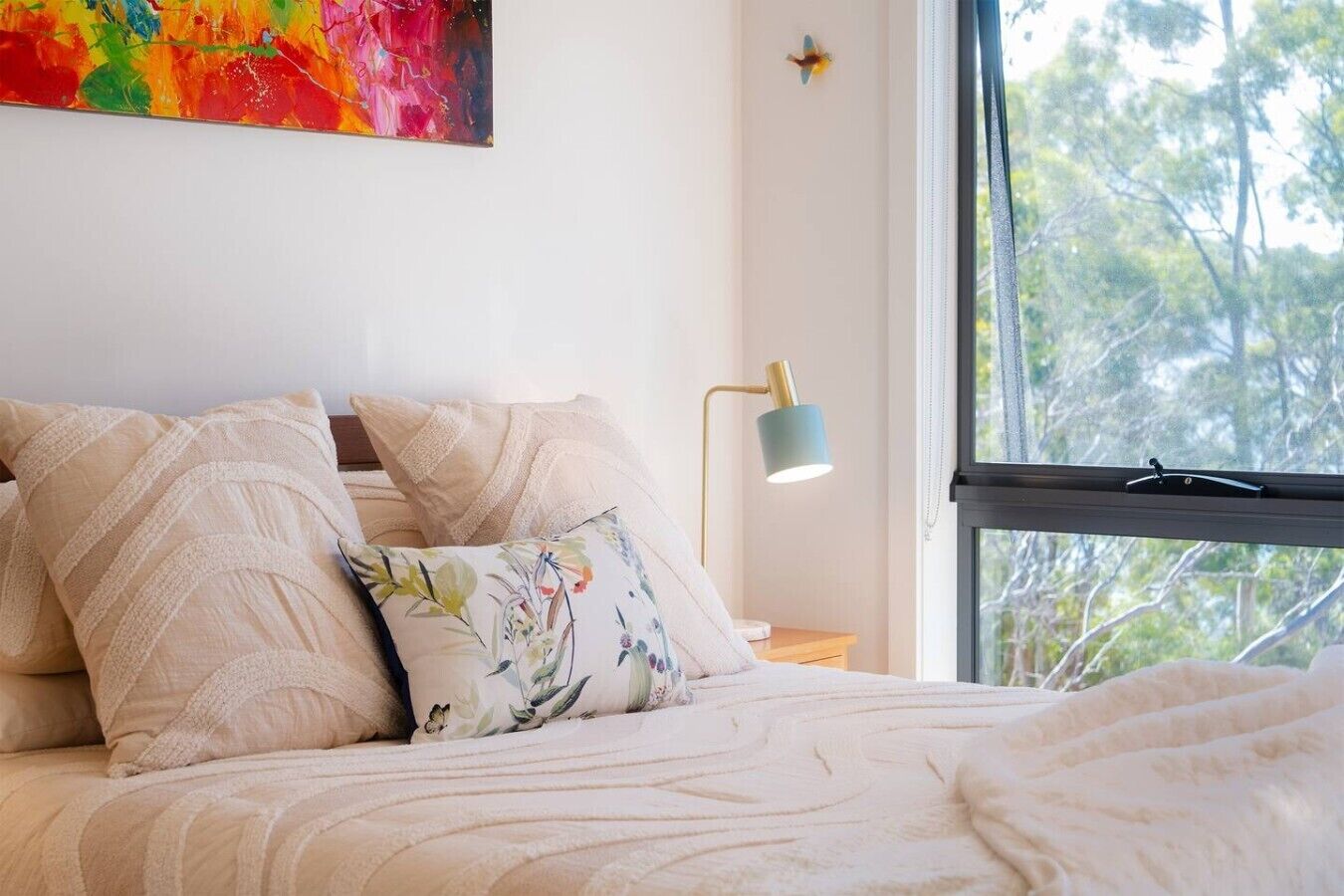 A bed with a floral pillow, a lamp, and a window with a view of trees.