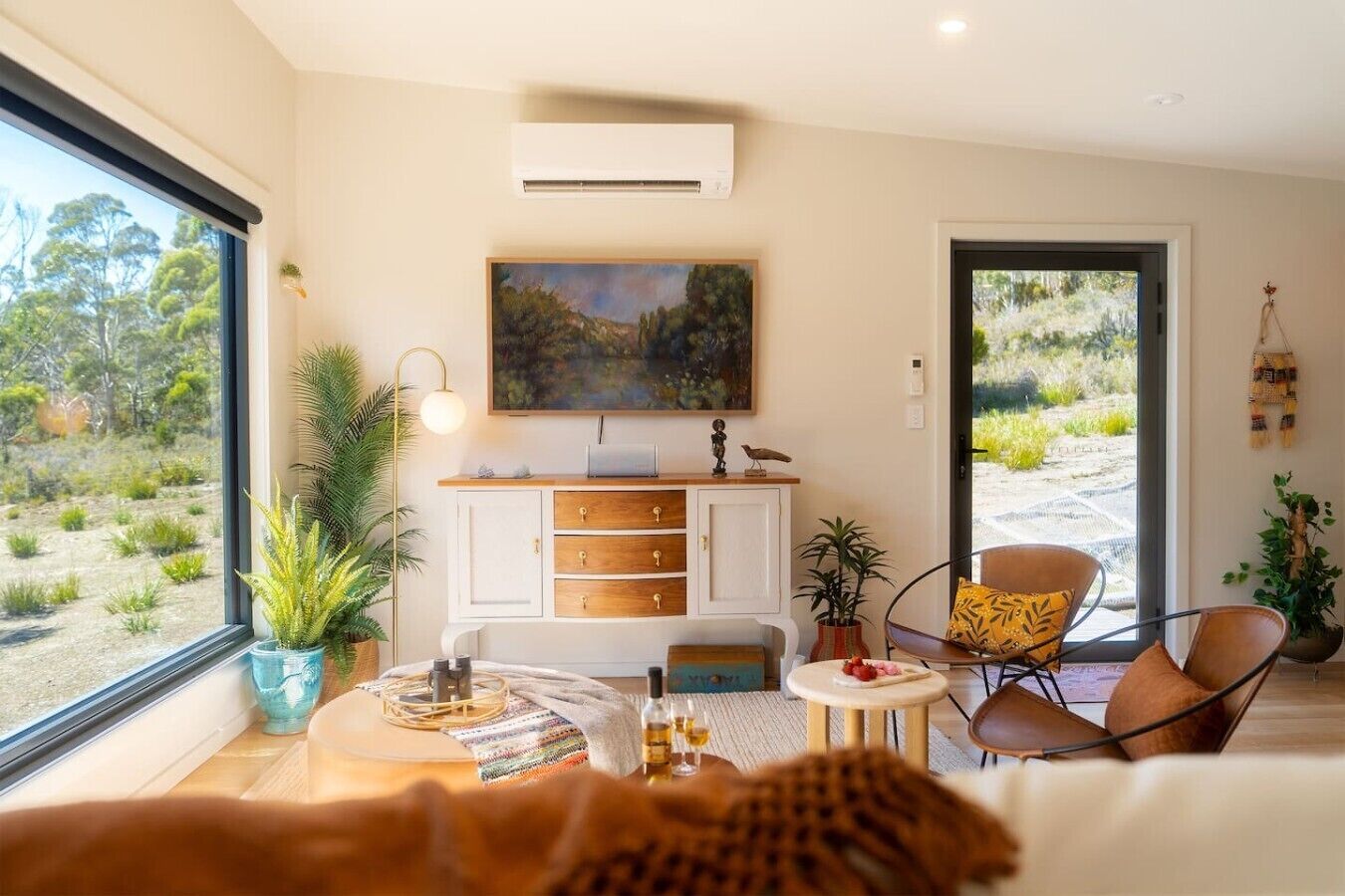 A modern room with a large window, a white cabinet, a painting, and a chair.