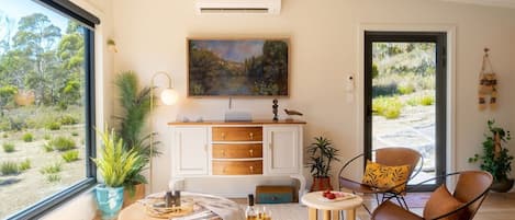 Une pièce moderne avec une grande fenêtre, un meuble blanc, un tableau et une chaise.