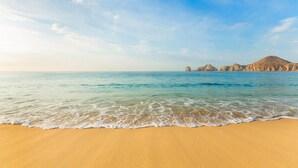 Ein Strand mit klarem Wasser, sandigem Ufer und Felsformationen im Hintergrund.