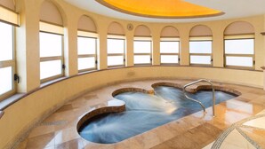 Ein Wellnessbereich mit Whirlpool, Bogenfenstern und Fliesenboden.
