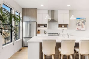 Una cocina moderna con una isla central, electrodomésticos de acero inoxidable, iluminación colgante y vistas al exterior.