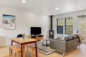 Una sala de estar con televisor, sofá, mesa de madera, banco, chimenea y ventanas.