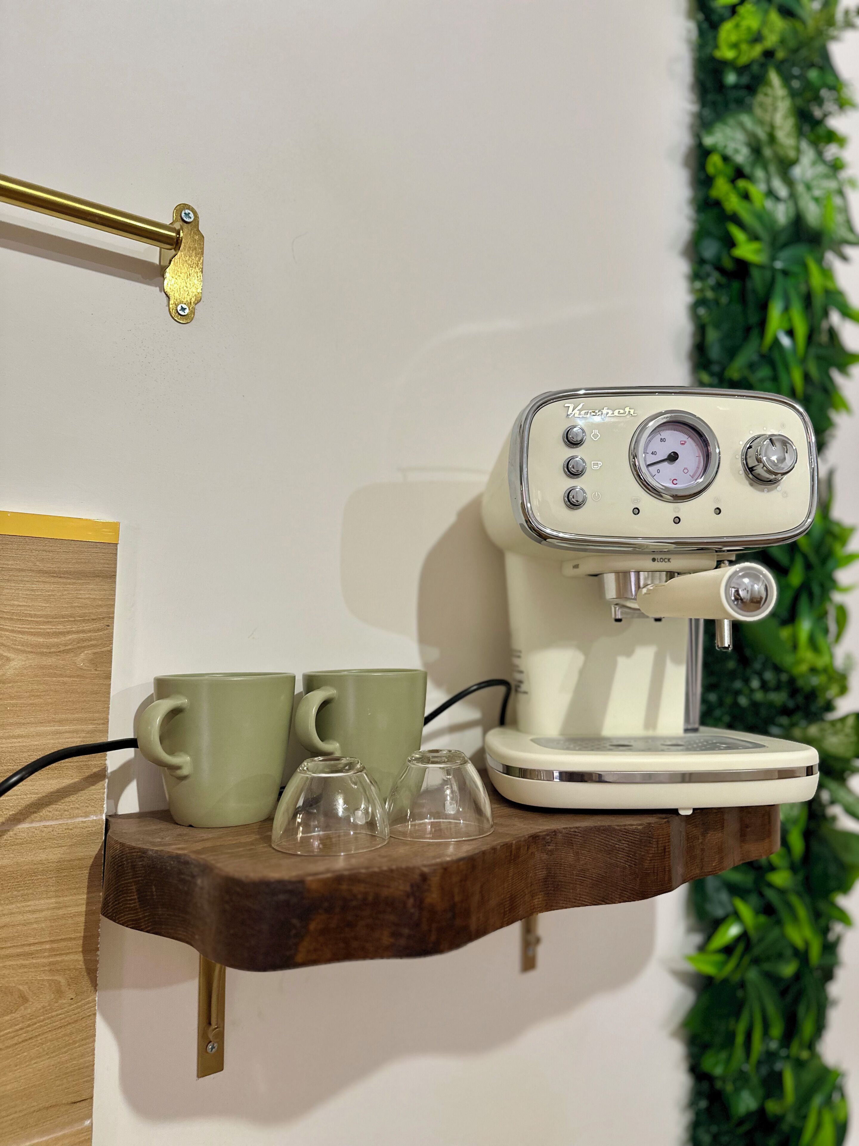 A coffee machine on a shelf with two green cups and two clear glasses.