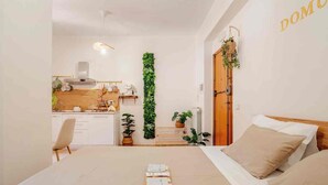 A bedroom with a bed, a bedside table, a wooden headboard, and a view of a kitchen and living area. - Domus Auri Vatican Jacuzzi Boutique Stay (Roma)