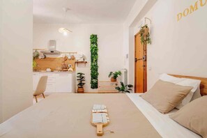A bedroom with a bed, a bedside table, a wooden headboard, and a view of a kitchen and living area. - Domus Auri Vatican Jacuzzi Boutique Stay (Roma)