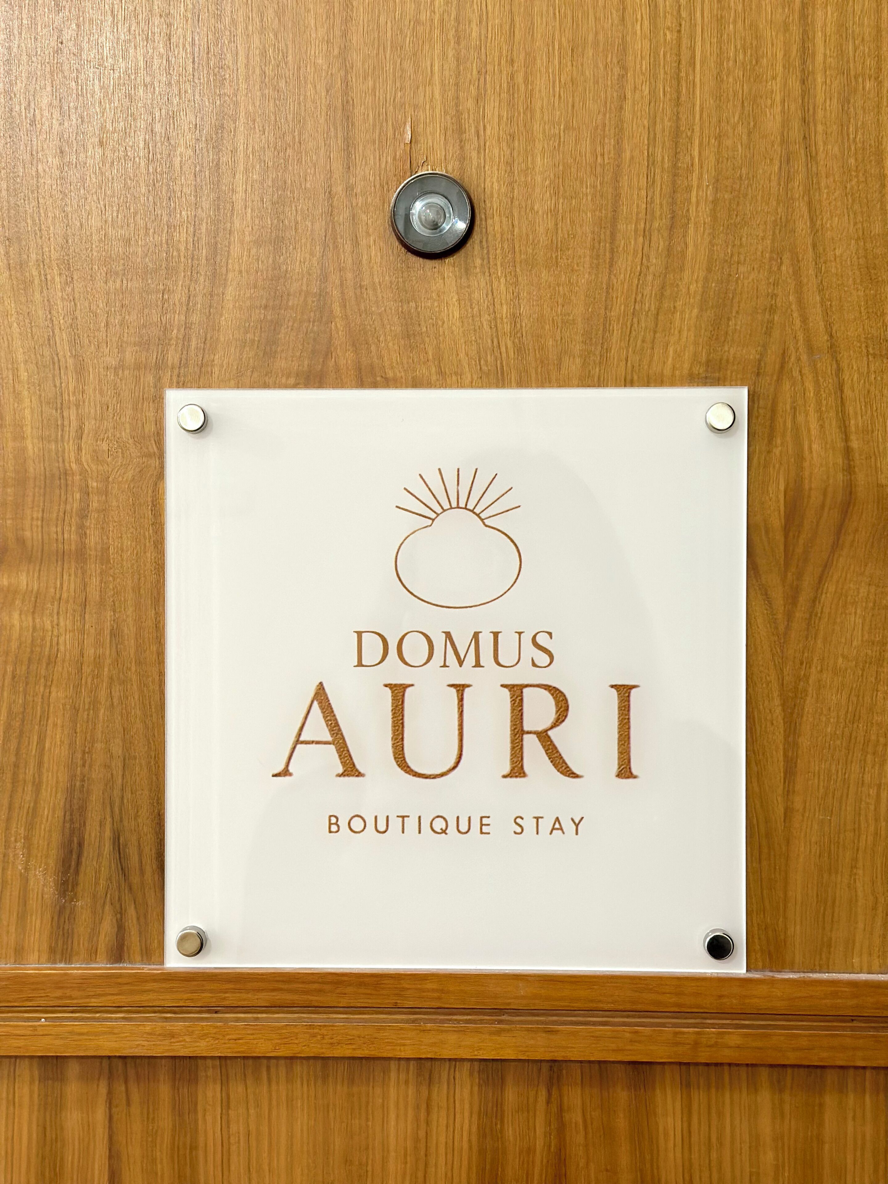 Ein Schild mit der Aufschrift 'DOMUS AURI' und 'BOUTIQUE STAY' an einer Holztür.