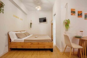 A bedroom with a wooden bed, a television, a dining area with a table and chairs, and a wall-mounted plant. - Domus Auri Vatican Jacuzzi Boutique Stay (Roma)