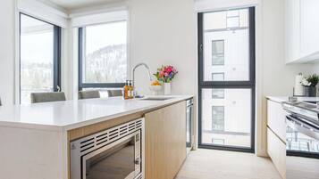 A modern kitchen with a central island, a built-in oven, and large windows offering views of the outdoors.