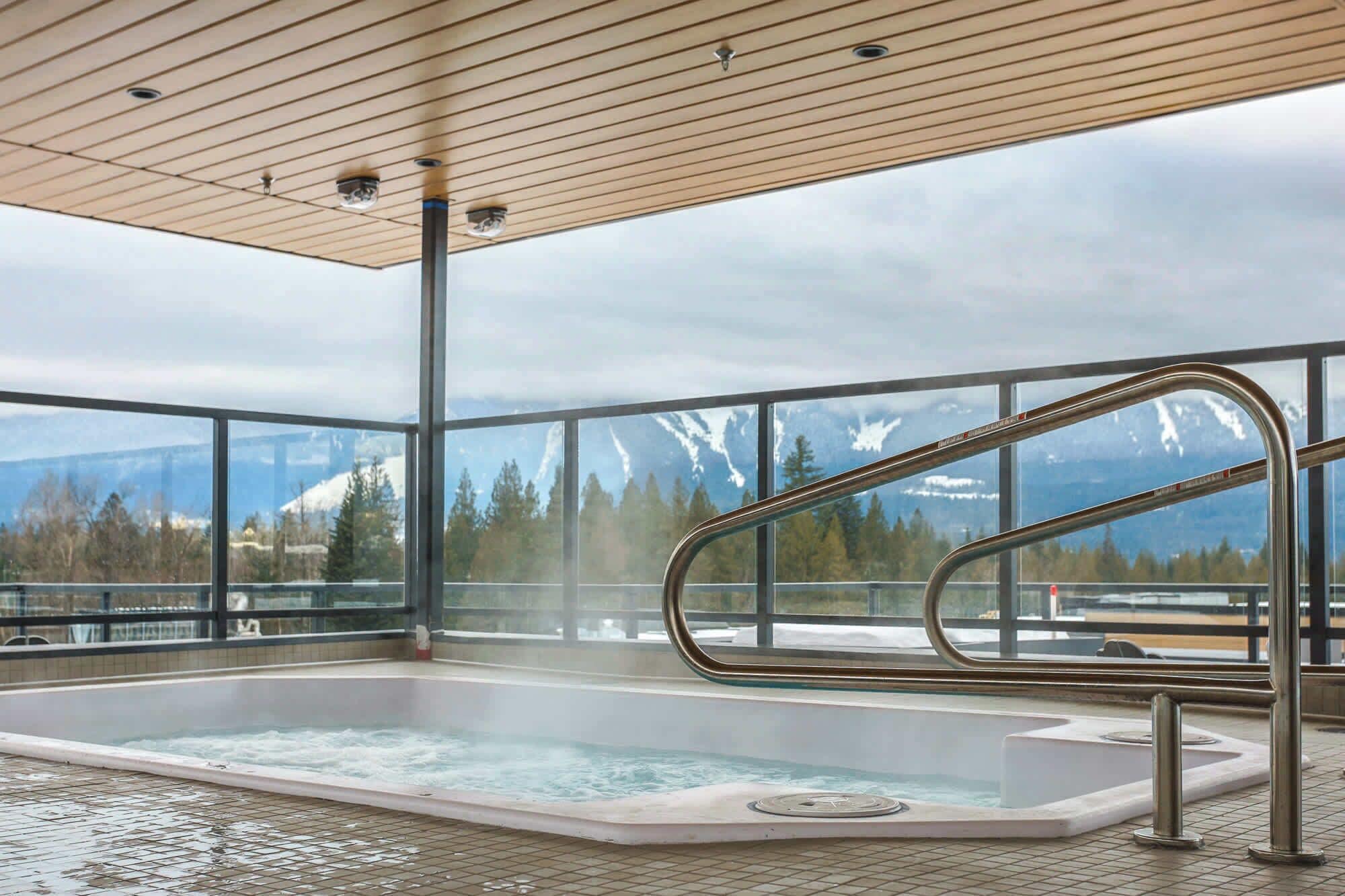 A hot tub with a view of snow-capped mountains, a wooden ceiling, and a metal railing.